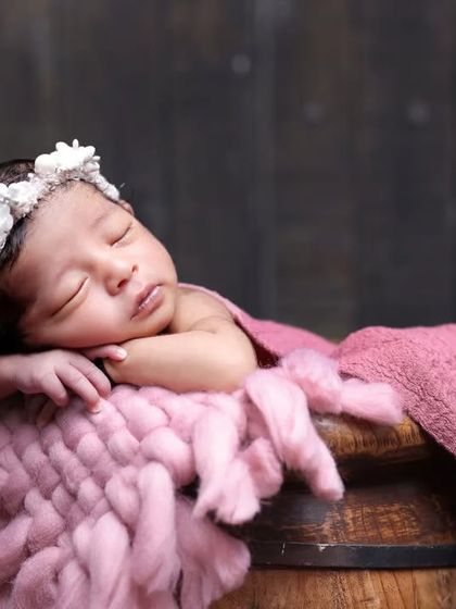 A close-up of the baby in the rustic floral bucket setup, highlighting the delicate flower crown and the soft, chunky knit fabric.