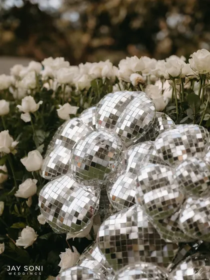 A cluster of disco balls nestled in a bed of classic white roses, a surprising and playful combination of textures and styles.