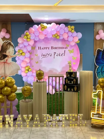 A beautiful, well-lit shot of the fairy and butterfly first birthday setup. The combination of a custom backdrop, gold chrome balloons, and whimsical cutouts creates a stunning visual.