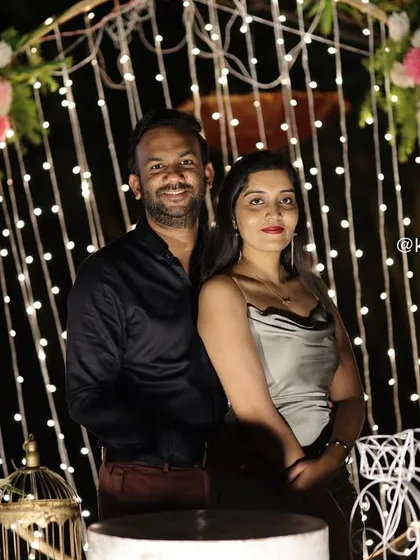 The happy couple posing at the "Bride to be" party. The warm lighting from the floral arch creates a cozy and celebratory setting for their photos.