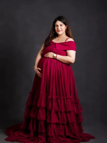A classic portrait showcasing a gorgeous, deep red tiered gown. The off-shoulder design and rich color beautifully complement the mom-to-be's radiant glow.