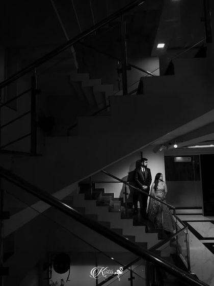 A wide black and white shot of a couple on a grand staircase, emphasizing the architecture and creating a sense of scale.