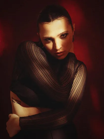 A moody and intimate portrait against a deep red background. The soft, directional light and the model's introspective pose create a sensual and mysterious atmosphere.