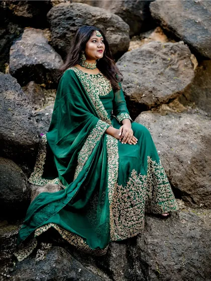 Seated among rocks, this portrait showcases the luxurious drape and intricate embroidery of the emerald green Anarkali.