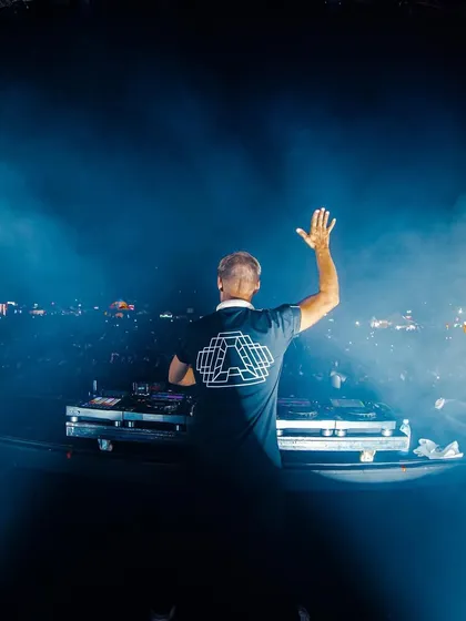 Armin van Buuren waves to the massive Bengaluru crowd from behind the decks, surrounded by a hazy blue atmosphere.