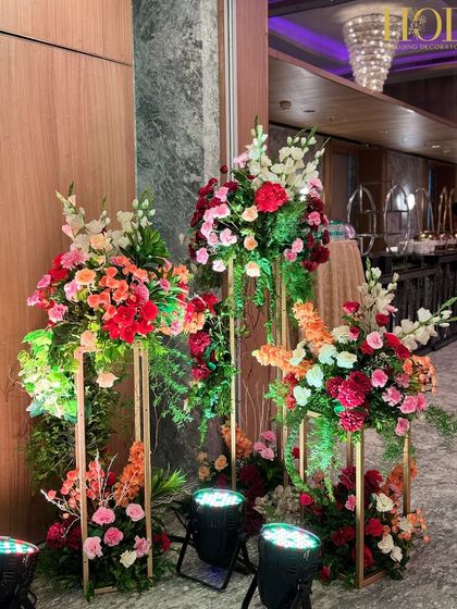 A beautiful floral arrangement on a modern gold stand, used as part of the entrance decor to add height, color, and a touch of contemporary elegance.