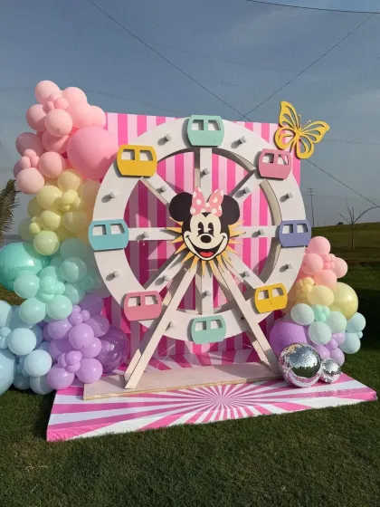 A cute Minnie Mouse ferris wheel prop, part of a larger carnival-inspired Disney party. The pastel balloons add a soft and dreamy touch.