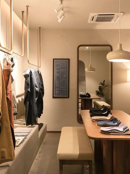 The retail display at Bombay Shirt Company, featuring custom brass hanging rails and integrated lighting. The design is clean and functional, allowing the texture and color of the garments to take center stage.