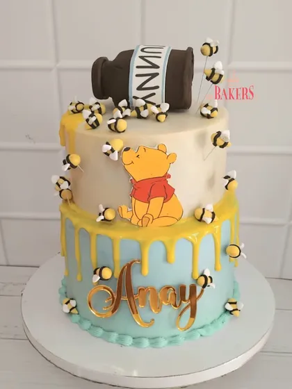 A sweet Winnie the Pooh cake for Anay's naming ceremony. This two-tier, no-fondant cake features Pooh Bear, a dripping "hunny" pot, and lots of busy little bees.