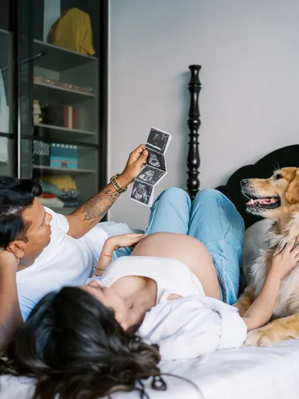 The whole family lies together on the bed, sharing the ultrasound pictures with their very attentive dog. It’s a beautiful, chaotic, and real moment of family life.