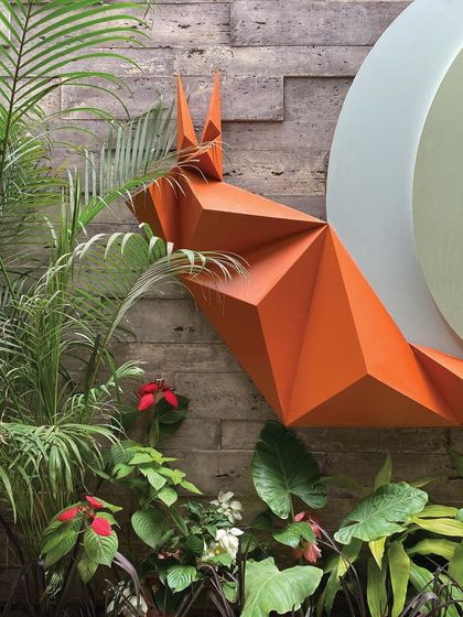 A close-up of the snail's form, showing the sharp, geometric folds of the metal contrasting with the soft, organic shapes of the surrounding plants. This juxtaposition is central to the piece's impact.