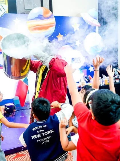 An entertainer performs a fun and smoky science experiment for a captivated audience of children at the space-themed party.
