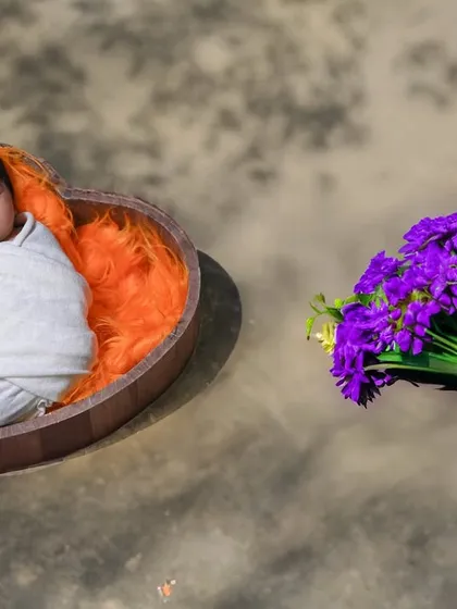 A simple yet beautiful Ugadi-themed shot, with a newborn in a heart-shaped bowl next to a bouquet of purple flowers.