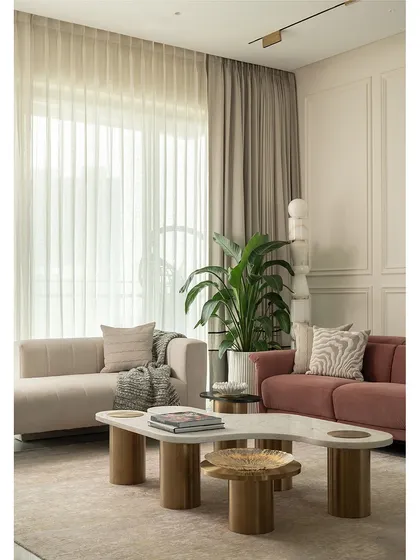 Natural light floods this living room, highlighting the soft textures of the rug and sofas. The layout is designed to be open and conversational, with a mix of curved and clean-lined furniture creating a balanced and harmonious feel.