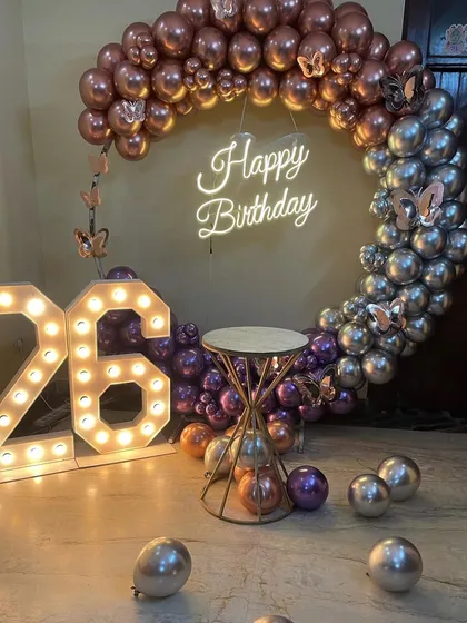 This is a duplicate of ID 37, 80, 136, 151, 158, 203, 247. A stylish half-arch balloon ring for a 26th birthday. This home decoration uses chrome rose gold and silver balloons, a neon sign, and marquee numbers.