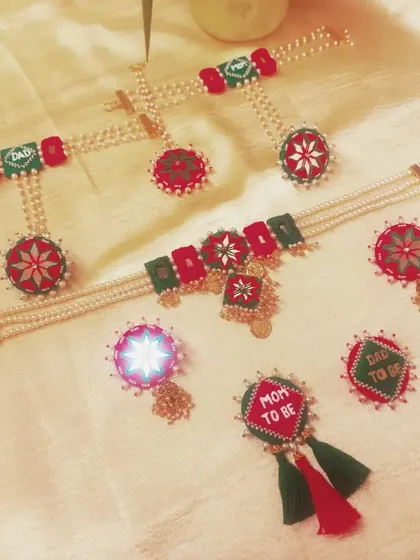 This is a complete baby shower jewelry set I created for a client. It includes a 'Mom to be' and 'Dad to be' brooch, necklace, earrings, and mathapatti, all handcrafted with fabric and pearls in a festive red and green theme.