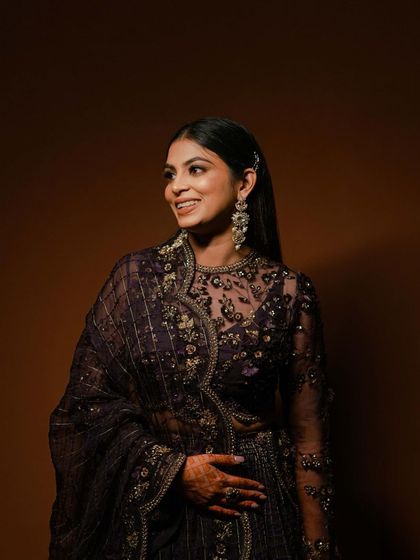A smiling portrait of the bride in a deep purple outfit, captured against a simple brown background to make her attire pop.