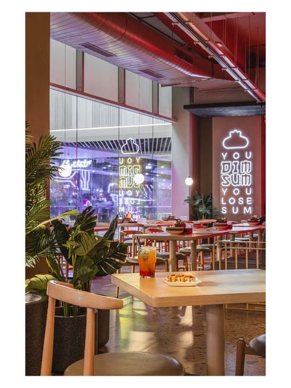 From this angle, the neon sign is visible from across the restaurant, acting as a beacon that draws the eye. The surrounding greenery provides a soft, natural contrast to the electric light.