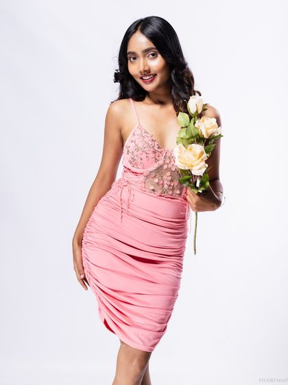 A full-body shot of the model in a pink dress, holding roses, with a joyful expression.