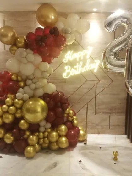 Celebrate turning twenty with a sophisticated balloon wall. This design uses a rich combination of burgundy, white, and chrome gold balloons, complemented by a glowing 'Happy Birthday' neon sign and large silver '20' number foils.