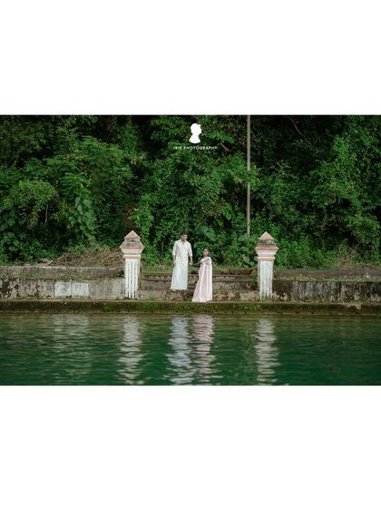 A wider shot of the couple by the temple pond, showing the beautiful green water and surrounding nature.