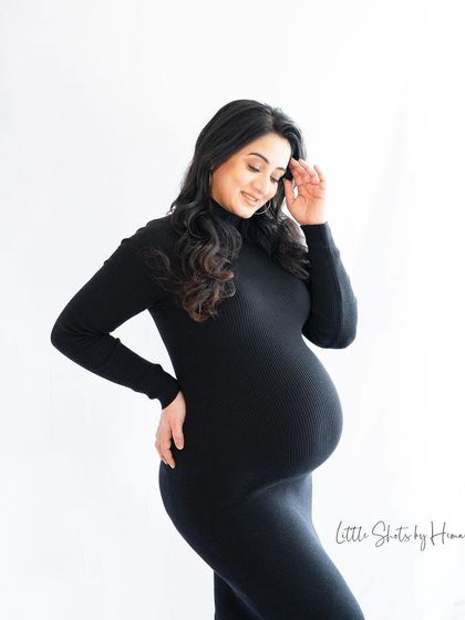 A simple yet elegant portrait of an expecting mother in a black dress. She stands in profile, smiling down at her bump, with the clean composition highlighting her beautiful silhouette.