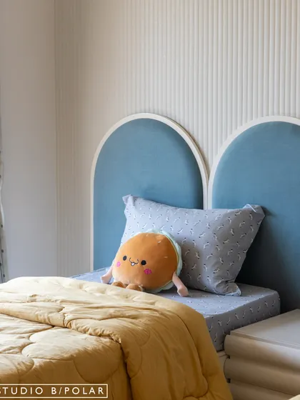 A close-up of the arched headboard and cute, plush toys that add to the room's playful character. The fluted wall paneling behind the bed adds a subtle layer of texture.