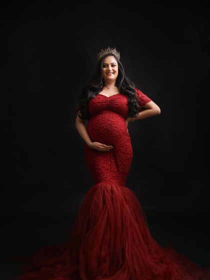 Radiant in red. This mom-to-be shines with confidence and joy in a stunning red lace gown, complete with a crown for a truly regal maternity portrait.