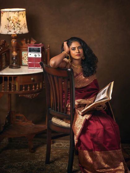 This portrait of Narayani is a complete scene, inspired by yesteryear paintings. Seated with a book, with a vintage radio and lamp beside her, she appears lost in thought. The warm, rich tones and carefully arranged props create a deeply nostalgic and narrative-rich image.