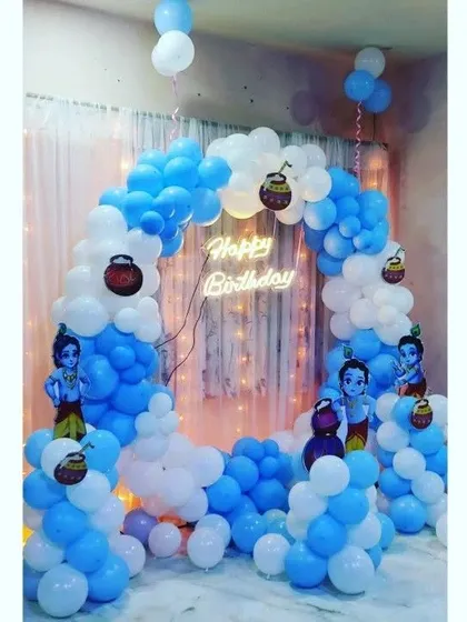 A divine Little Krishna themed decoration, using a blue and white balloon arch, cutouts of Krishna, and small 'matki' props.