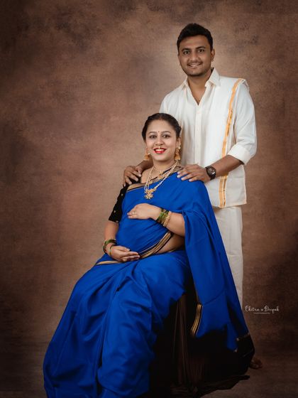 A classic seated portrait of a couple in traditional attire. The rich blue of her saree provides a stunning pop of color.