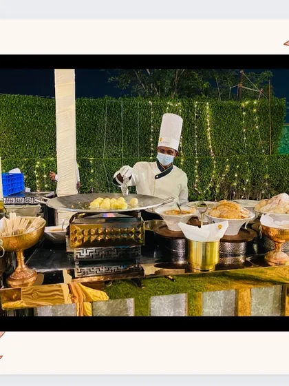 A chef at a live chaat counter preparing plates of bhalle papdi for guests at an outdoor evening event.