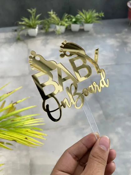 Announce your bundle of joy with this adorable "Baby On Board" cake topper. Featuring cute baby feet icons, it's the perfect centerpiece for your baby shower cake, shown here in a classic gold mirror finish.
