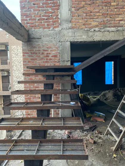 The structural form of a cantilevered metal staircase under construction. This element is as much a piece of sculpture as it is a functional staircase.