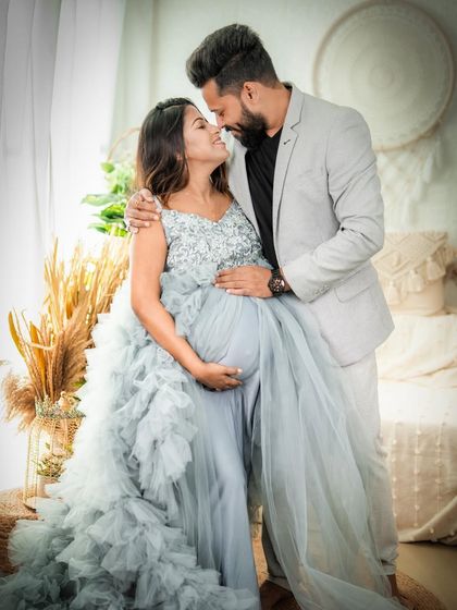 A fairytale romance. This couple shares an intimate moment, with the mom-to-be in a flowing blue gown and her partner in a sharp suit, creating a glamorous and loving portrait.