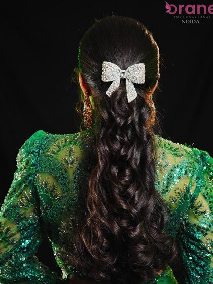 A chic and simple half-up hairstyle with voluminous curls, accented with a sparkling bow.