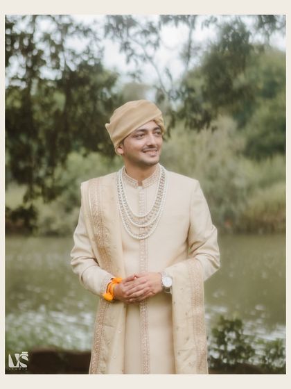 A classic, smiling portrait of the groom, Mrityunjay, set against a serene natural backdrop. It's a timeless shot that captures his happy and calm demeanor on his wedding day.