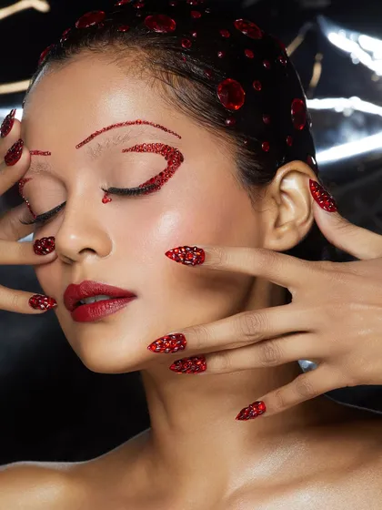 A stunning monochromatic red look, featuring red glitter brows, eyes, and lips, with matching red crystal nails.
