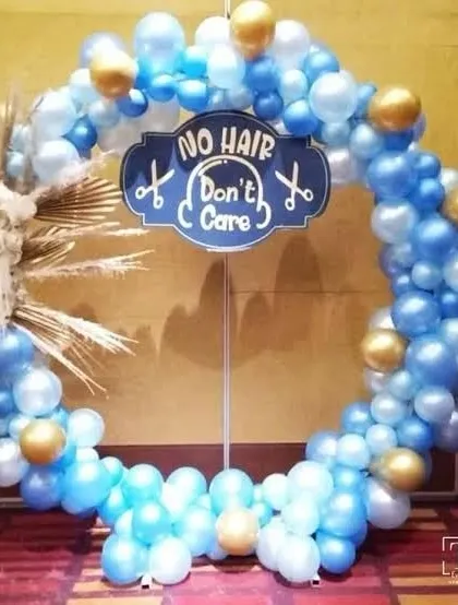 A fun and unique backdrop for a baby's mundan or first haircut ceremony, with a 'No Hair Don't Care' sign on a blue and gold balloon ring.