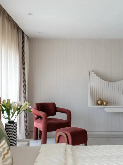 This view of the parent's bedroom highlights the elegant reading nook. The combination of the comfortable armchair, the sculptural wall shelf, and the soft lighting creates a perfect spot to unwind with a book.