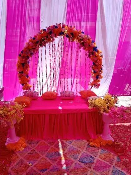 I can create a cozy and vibrant Mehndi setup inside a tent. This one features a floral arch over a low seating arrangement, all in a bright pink theme.