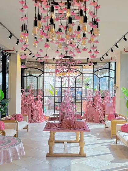An elegant bridal shower bathed in blush pink. The space is illuminated by custom chandeliers dripping with pink flowers and Edison bulbs, creating a romantic and modern ambiance for the bride-to-be.