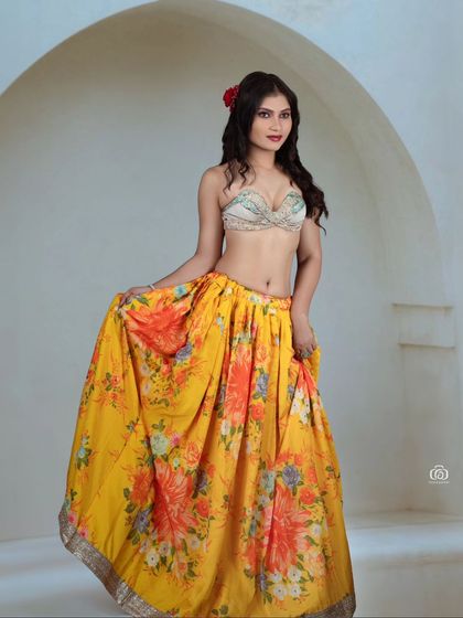 A full-length view of a model in a bright, floral-patterned skirt and embellished top. The clean studio background allows the colorful outfit to take center stage.