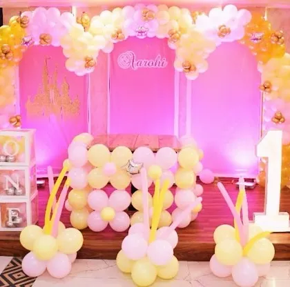 The main stage for the princess party, decorated in shades of pink and yellow with a balloon arch and character cutouts.
