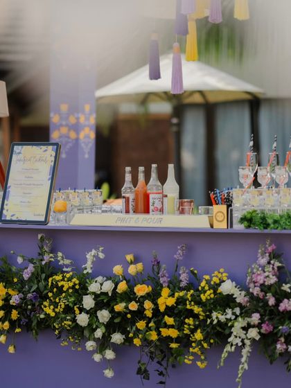 A detail shot of the Haldi cocktail bar, showcasing the fresh floral runner and the curated selection of colorful syrups and drinks.