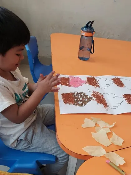 A young boy carefully adding materials to his cupcake artwork. This activity encourages fine motor skills and decision-making as he chooses which textures to use.