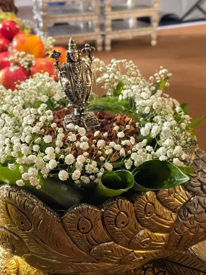 A beautiful offering of betel nuts and leaves with a small silver deity, arranged in a brass peacock bowl with baby's breath.
