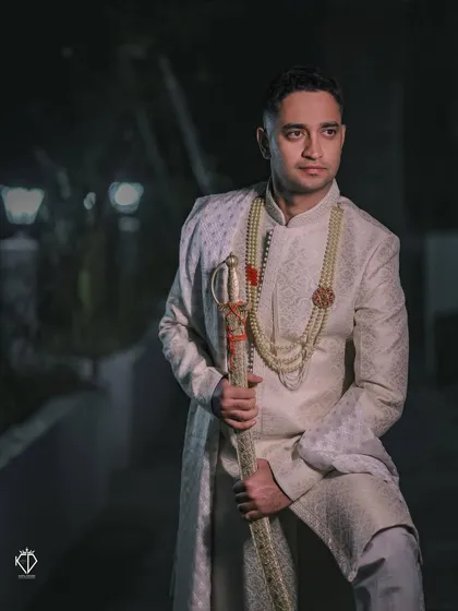 A stylish portrait of the groom in his off-white sherwani, captured in the soft evening light. The mood is classic and contemplative.
