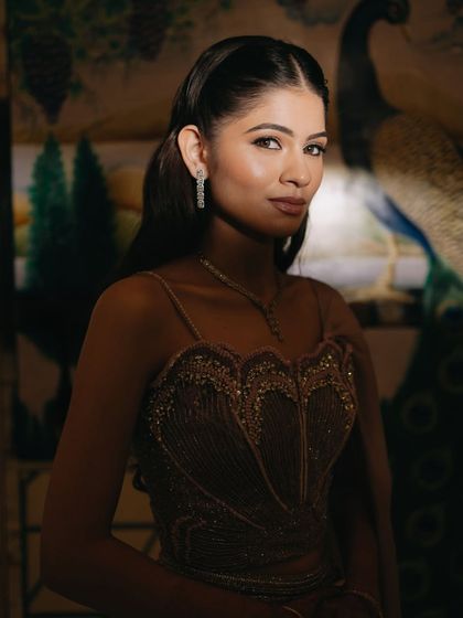 A close-up bridal portrait with a peacock mural in the background, the soft lighting highlighting her delicate features and jewelry.