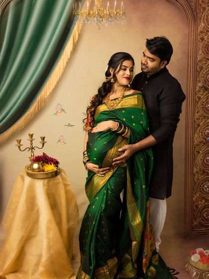 A beautiful couple's portrait from a twin pregnancy photoshoot. The deep green of the saree contrasts wonderfully with the classic painterly backdrop, creating a truly artistic memory.